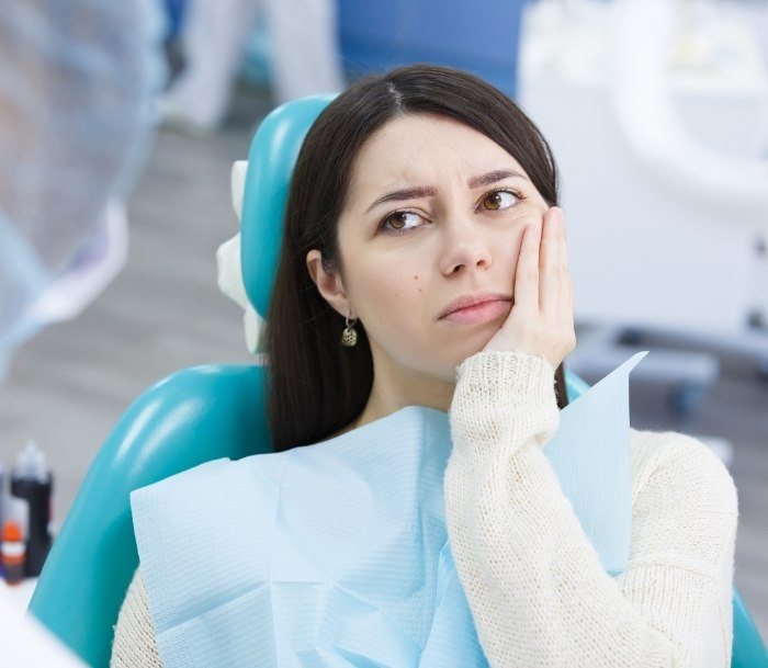 Woman in dental chair holding her cheek in pain before apicoectomy in Paramus