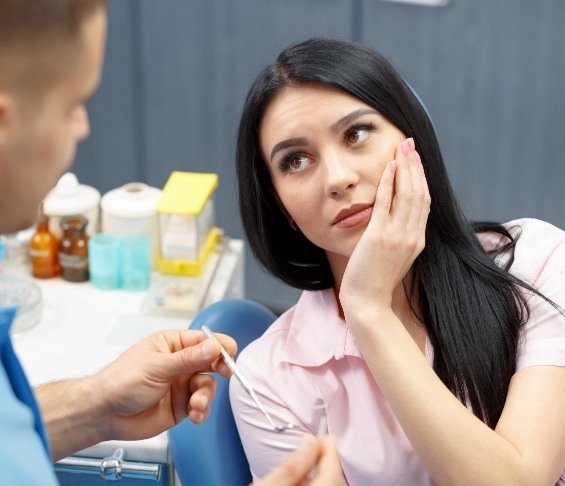 Woman in dental chair holding her cheek in pain