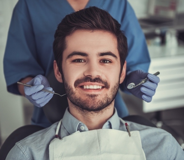 Young man with short facial hair smiling in dental chair